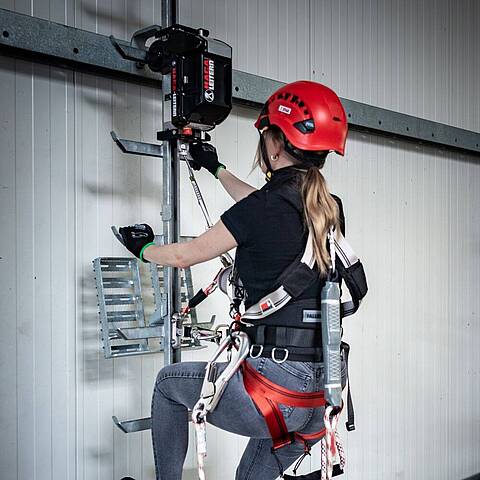 A woman climbing in an industrial hall with a climbing aid made by HACA Leitern