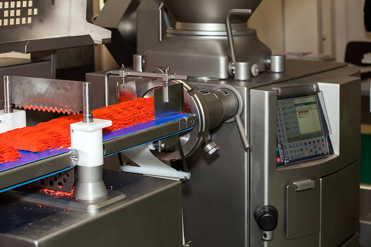 Industrial meat mincer produces minced meat and places it in portions on a conveyor belt