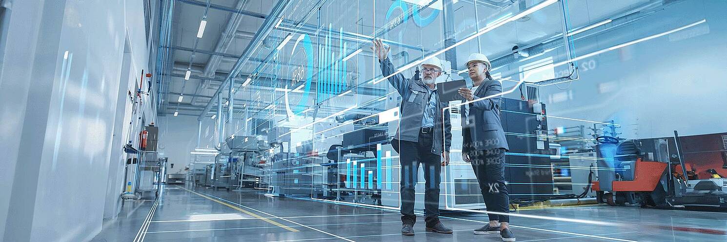 man and woman with safety helmets on in a production hall, looking at a virtual HMI dashboard