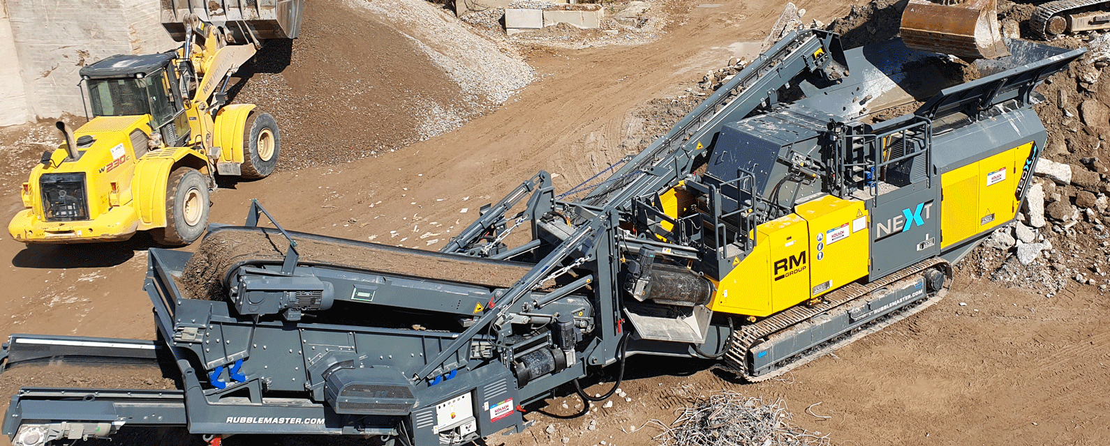A mobile Crusher manufactured by RubbleMaster in action on a working site with a wheel loader