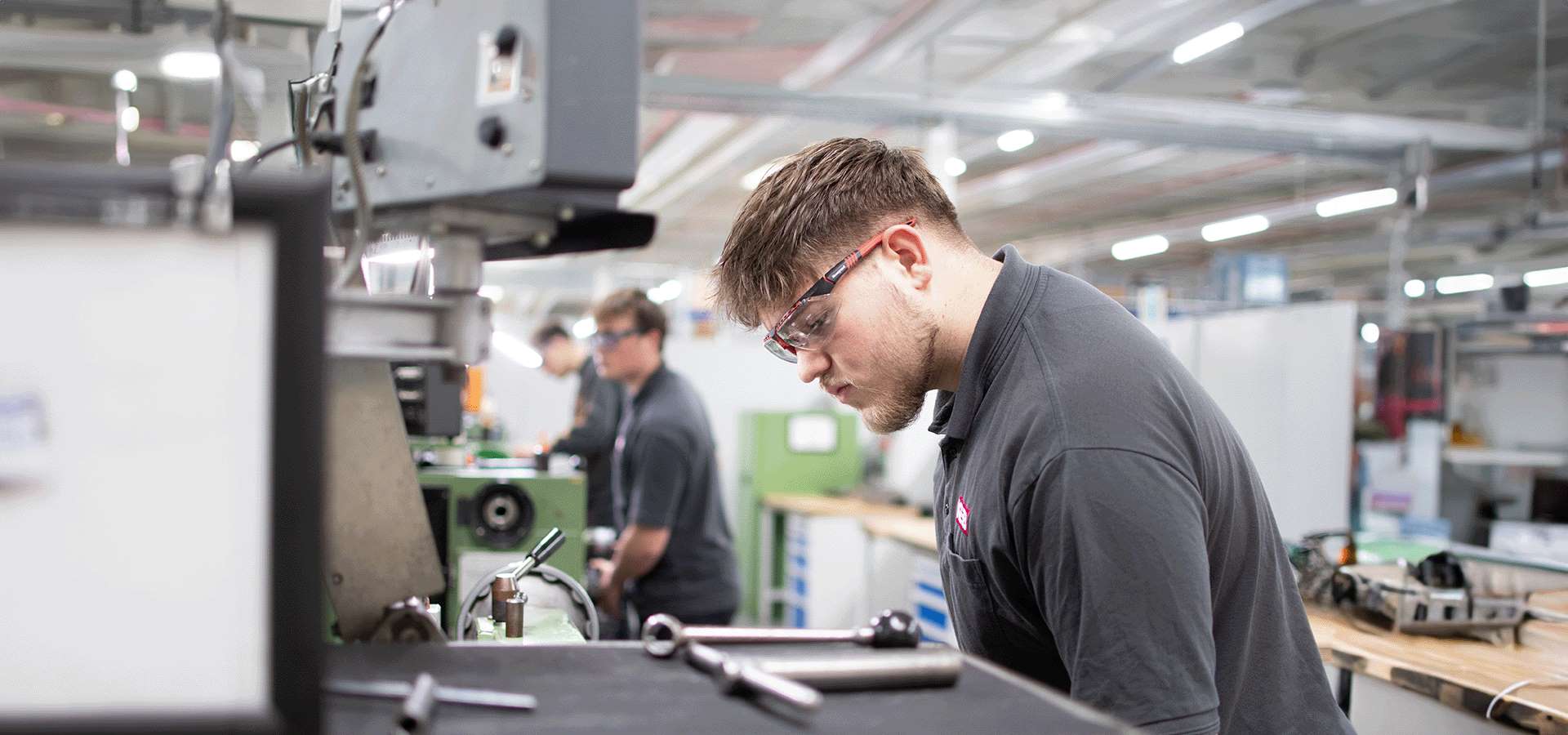 Junger Mann (Auszubildender bei KEB Automation) bei der Arbeit an einer Metallbearbeitungsmaschine, im Hintergrund andere, die dasselbe tun.